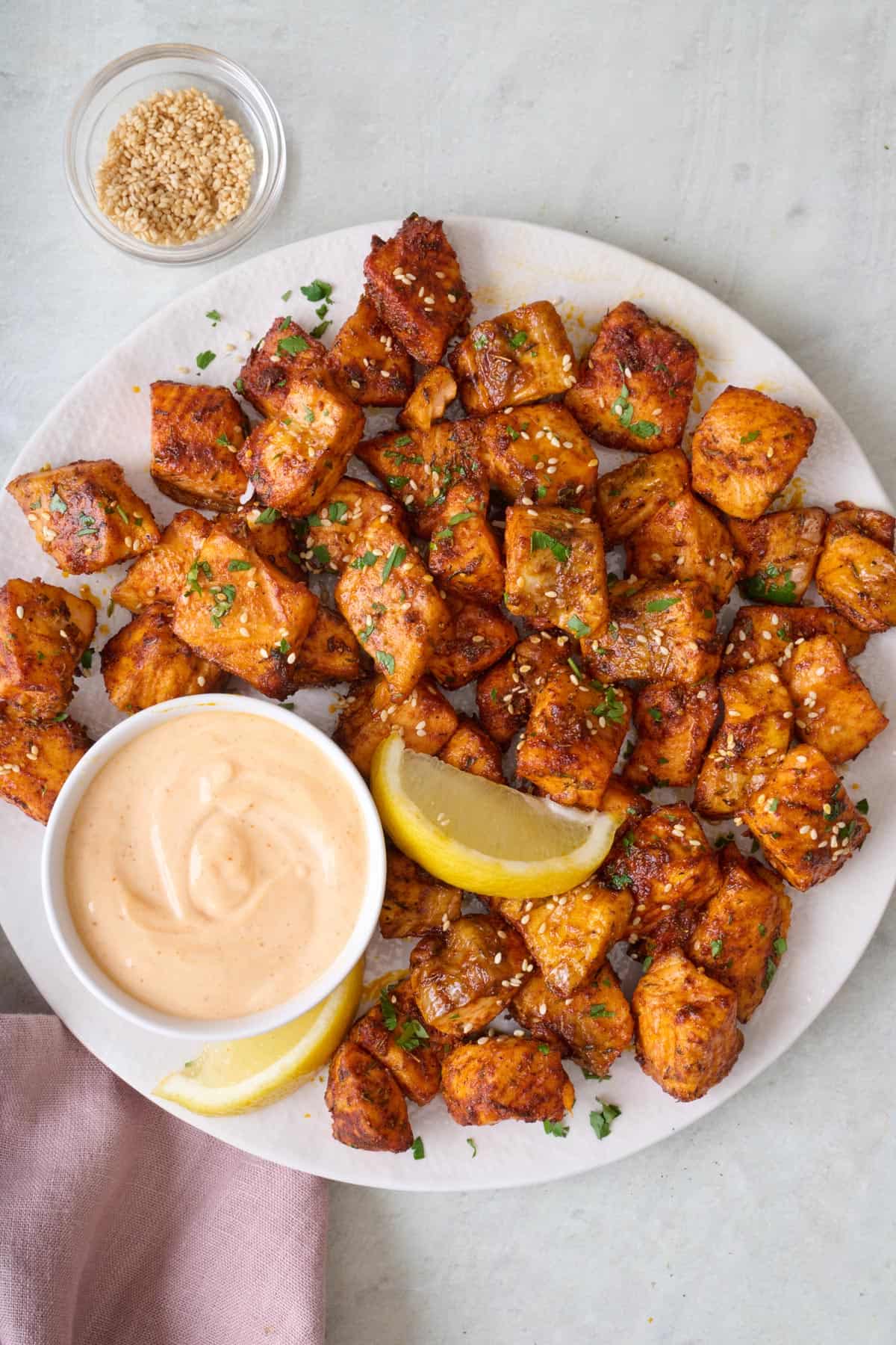 Air fryer salmon bites on a plate with spicy mayo for dipping and garnished with sesame seeds.