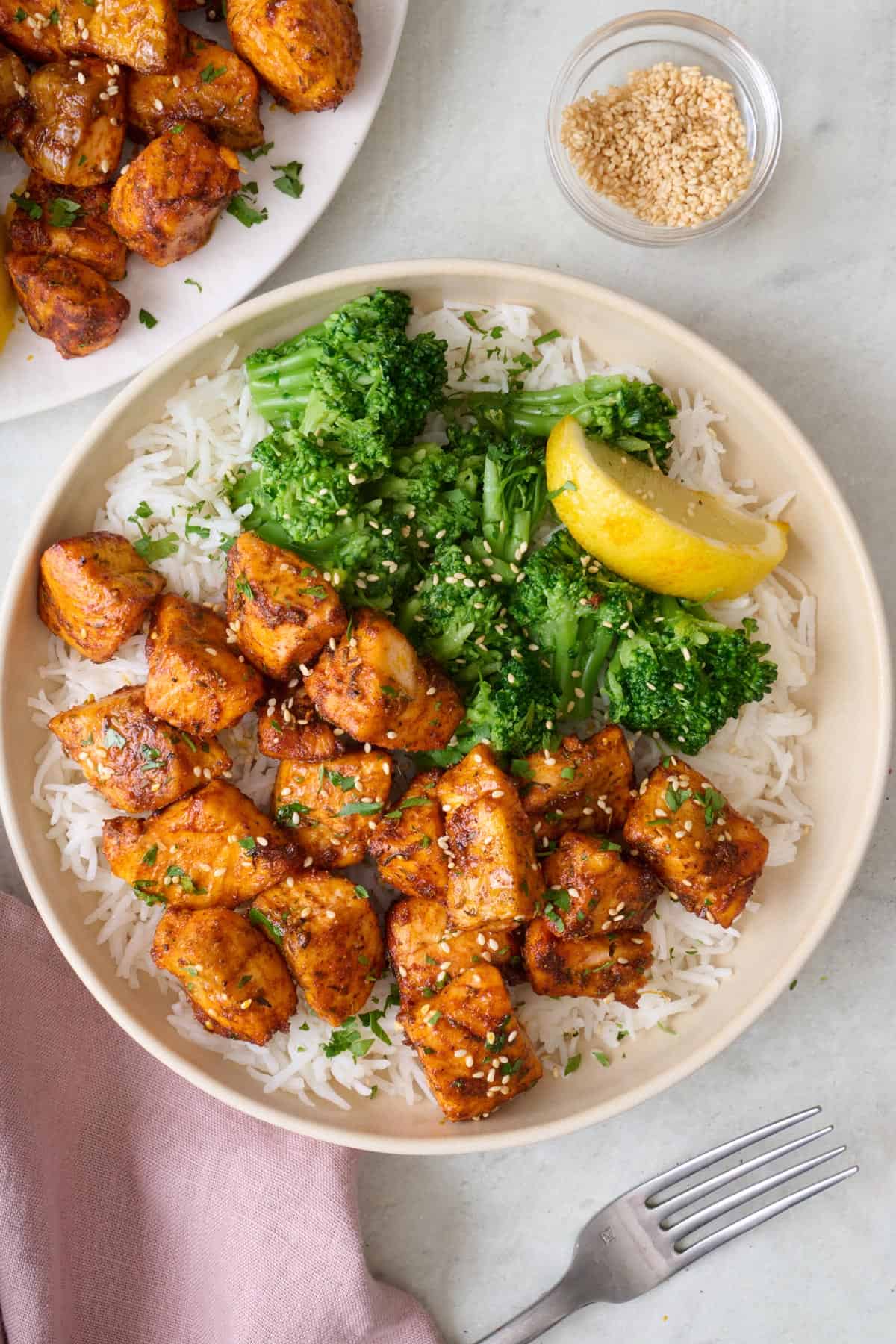 A bowl of rice topped with crispy air fried salmon pieces and broccoli, topped with sesame seeds.