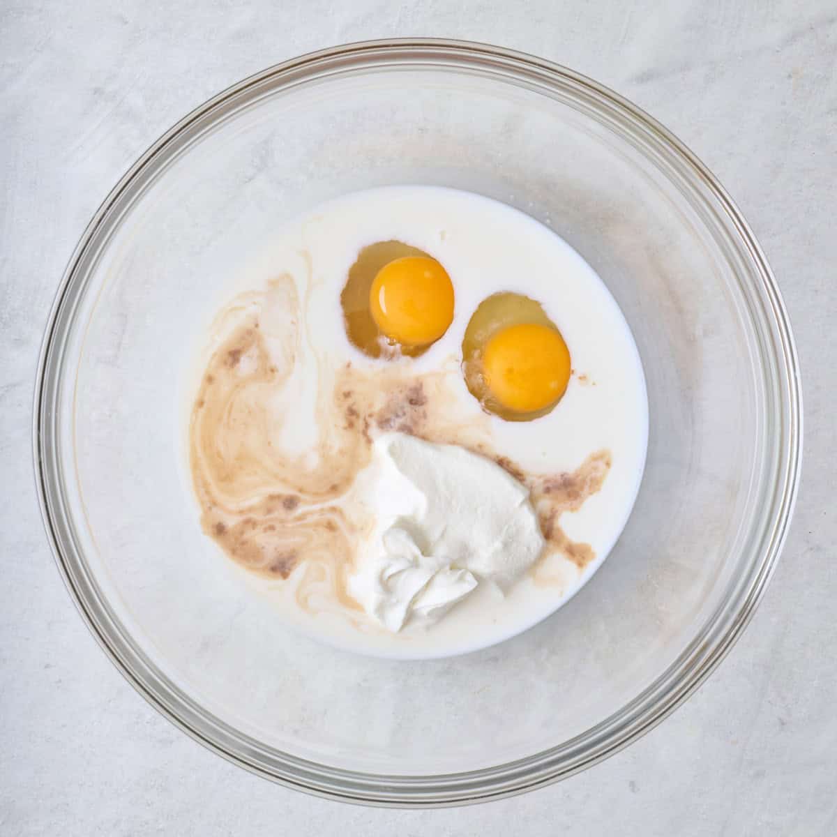 Eggs, yogurt, milk, maple syrup and vanilla in a bowl.