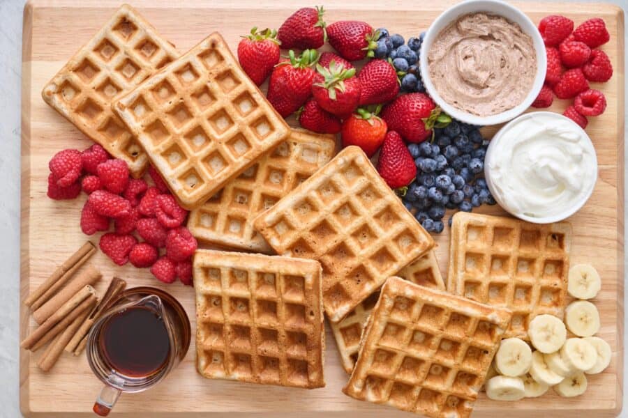 pile of waffles on a cutting board with fruit, cinnamon butter and syrup for Mother's Day Brunch