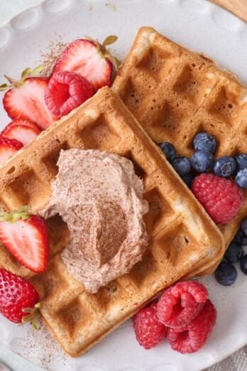Cinnamon waffles on a plate with whipped cinnamon butter and fresh fruit.