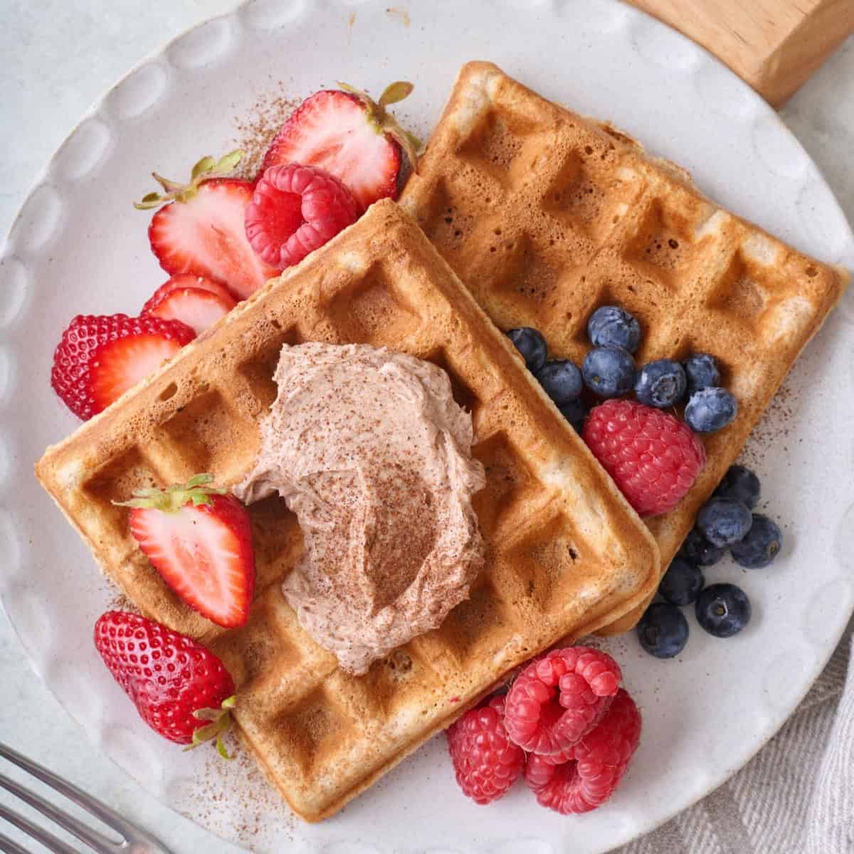 Cinnamon waffles on a plate with whipped cinnamon butter and fresh fruit.