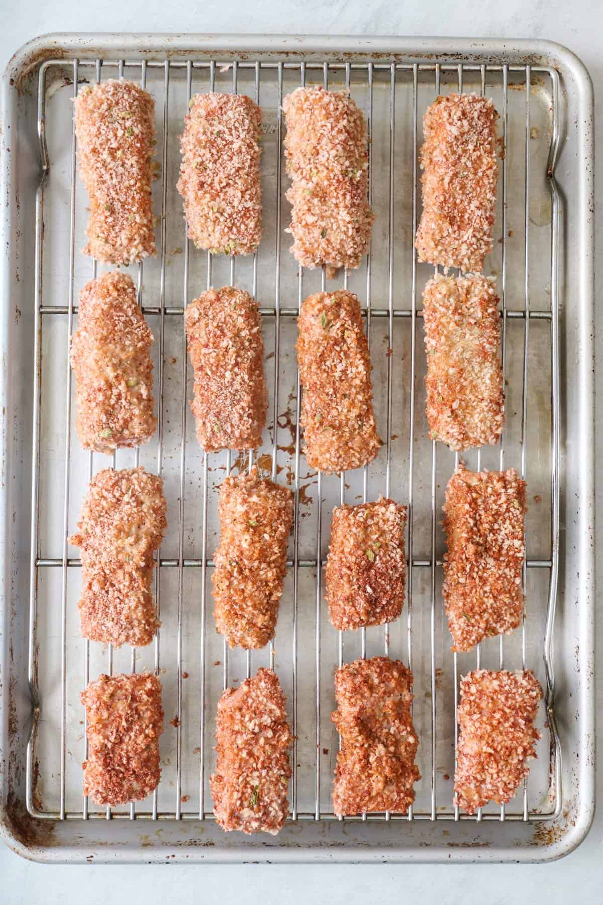 Breaded salmon pieces on a wire rack on top of a sheet pan before baking.