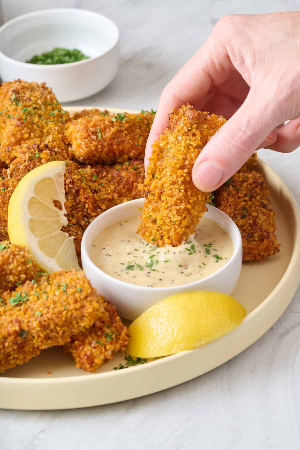 Hand dipping a salmon fish stick into a creamy sauce.