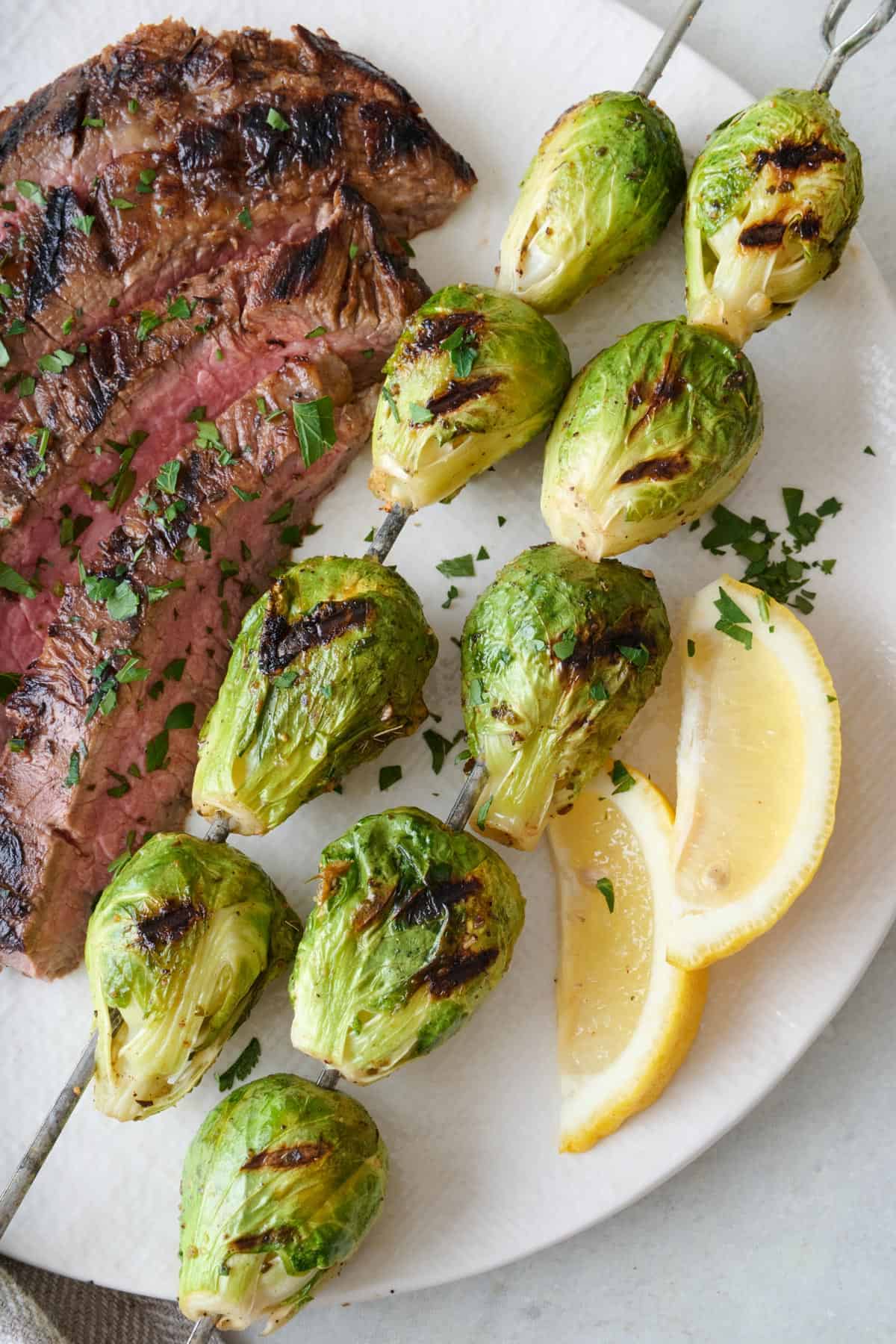 Two brussel sprouts skewers on a plate with sliced steak.