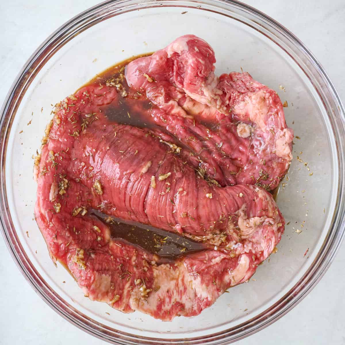 Flank steak in a bowl of marinade.