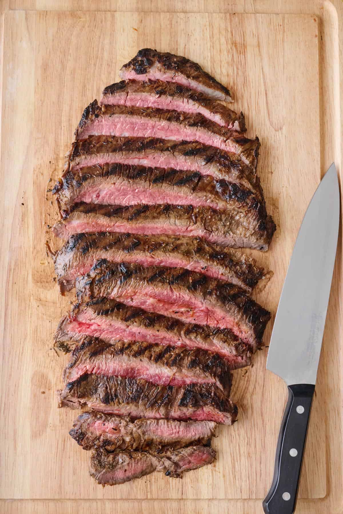 Flank steak on a cutting board after grilling and cut into thick slices.
