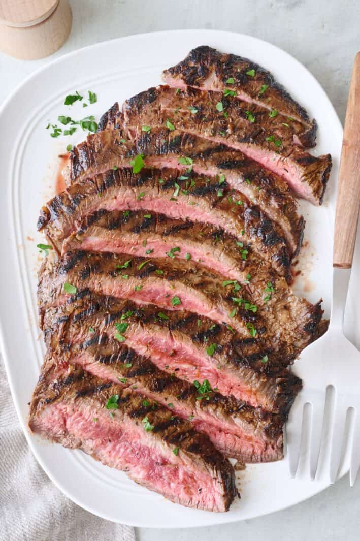 Grilled flank steak slices fanned out on a large platter.