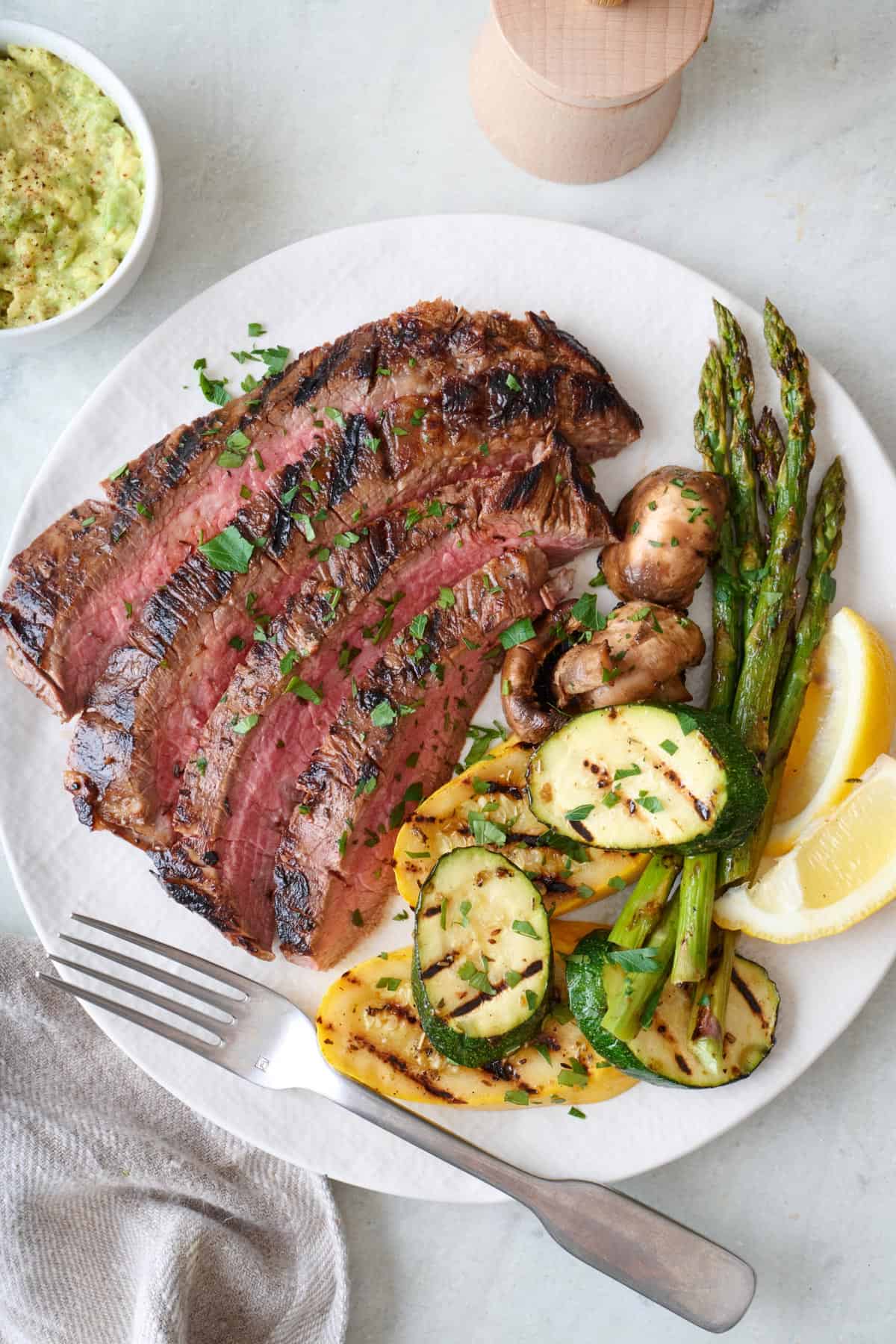 Grilled flank steak on a plate with grilled vegetables.