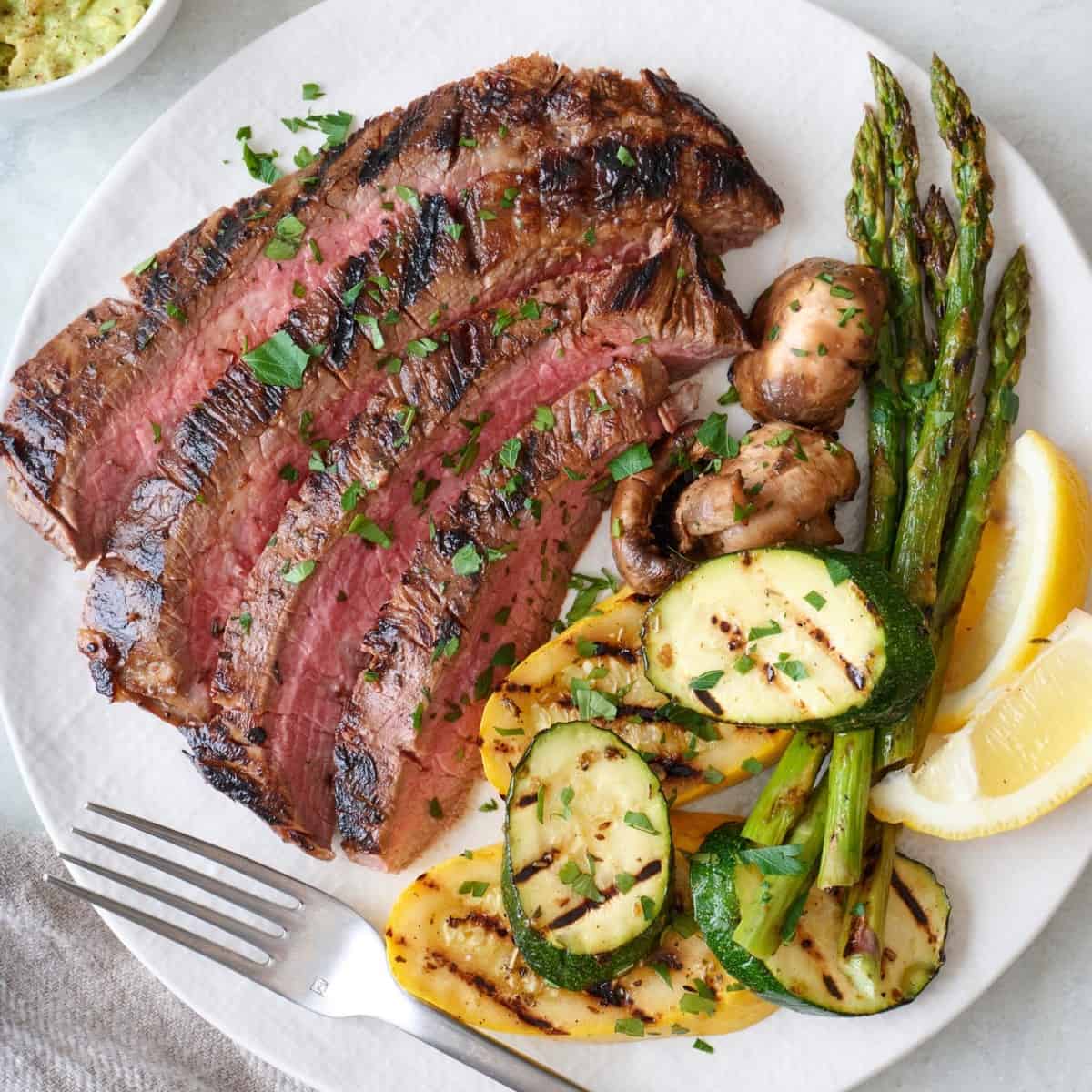 Sliced flank steak on a plate with grilled veggies.