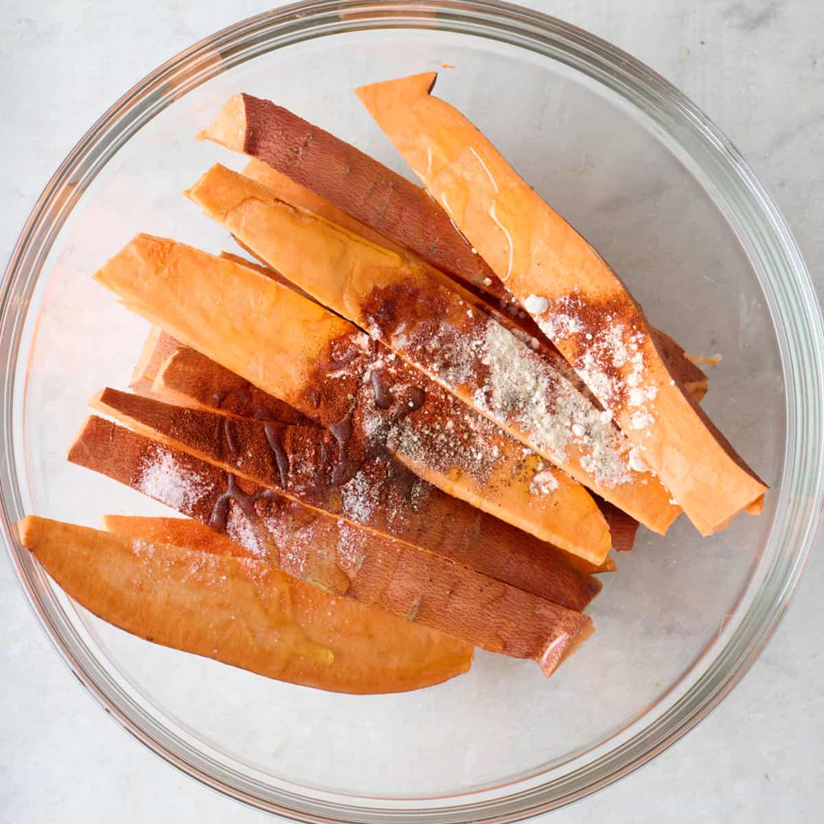 Sweet potato wedges in a bowl with oil and seasoning, before tossing together.