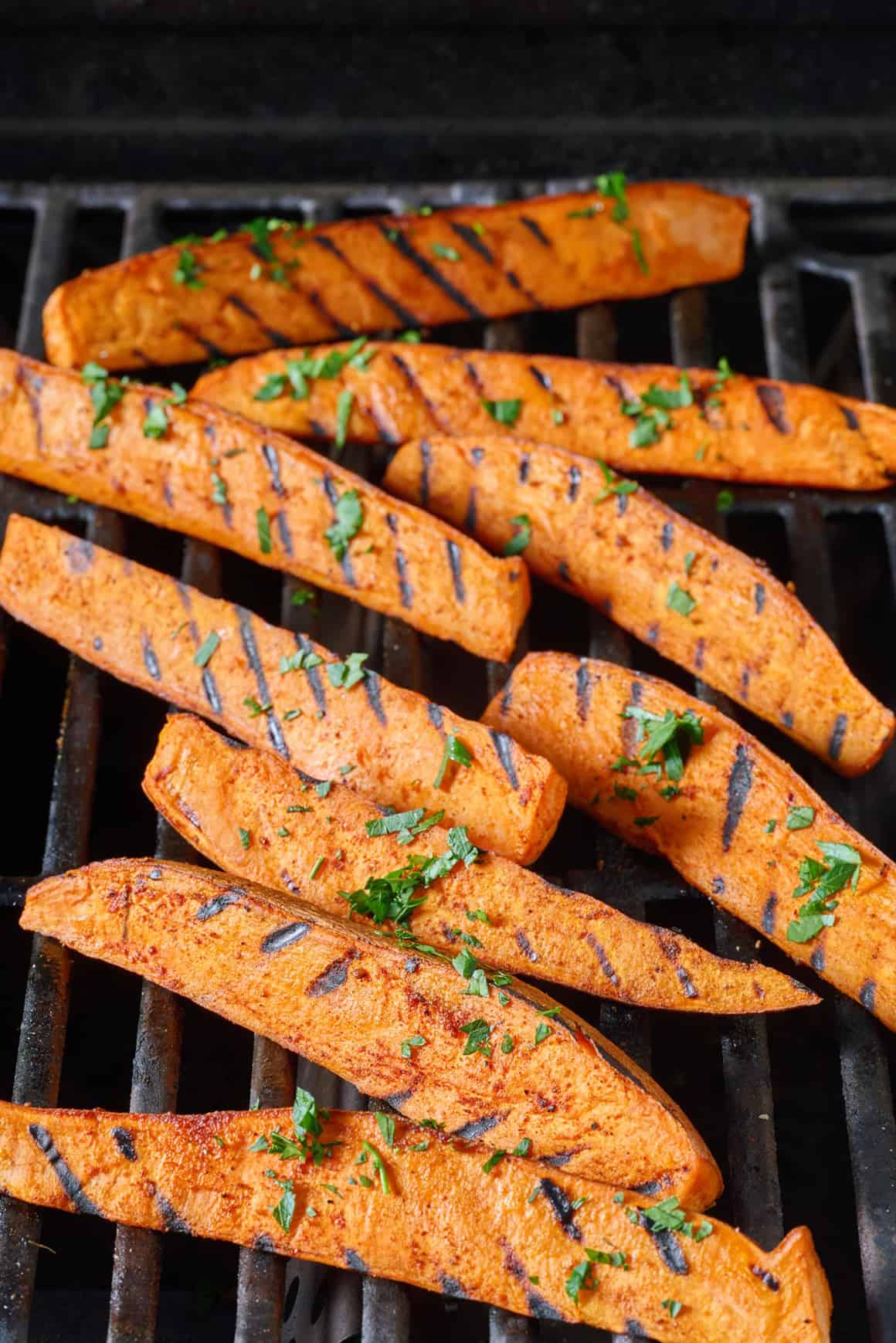 Grilled sweet potato wedges on an outdoor grill, garnished with fresh parsley.