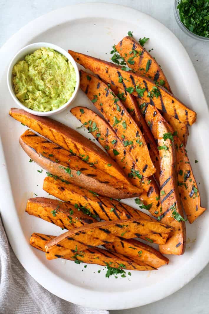 Grilled sweet potato wedges on a large platter with sauce for dipping.