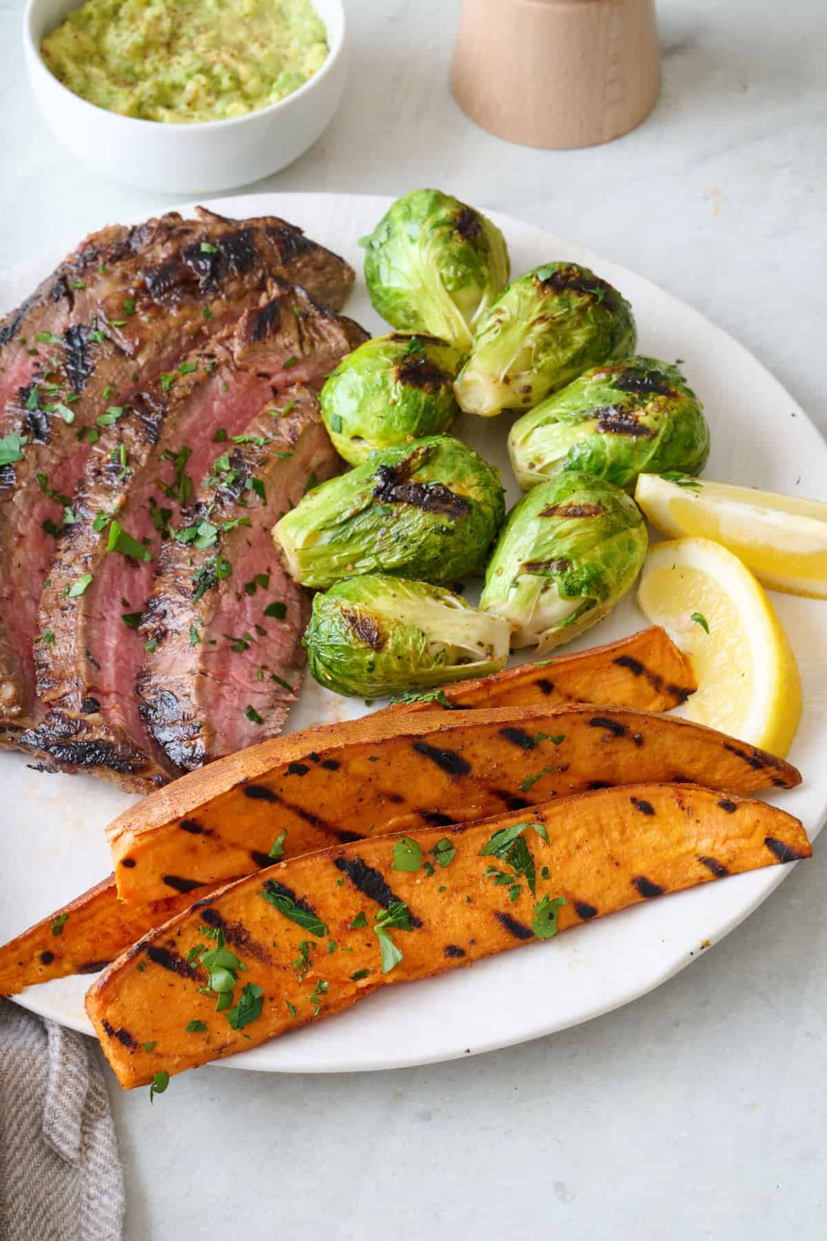 Grilled sweet potato wedges on a plate with sliced grilled steak and brussel sprouts.