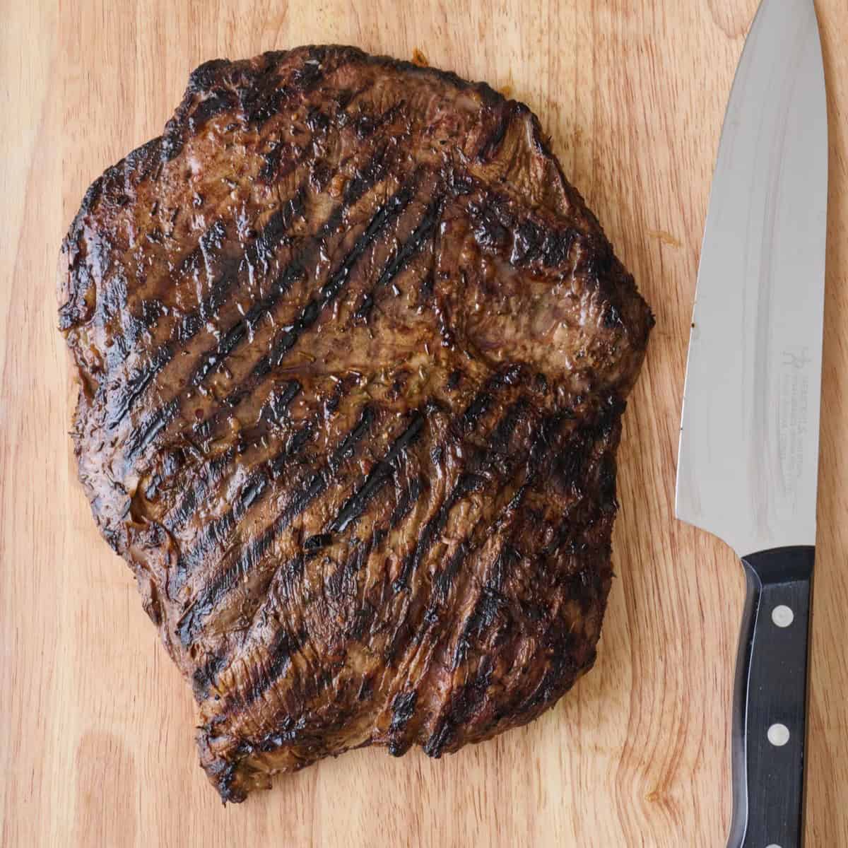 Grilled flank steak on a cutting board with a chef's knife.