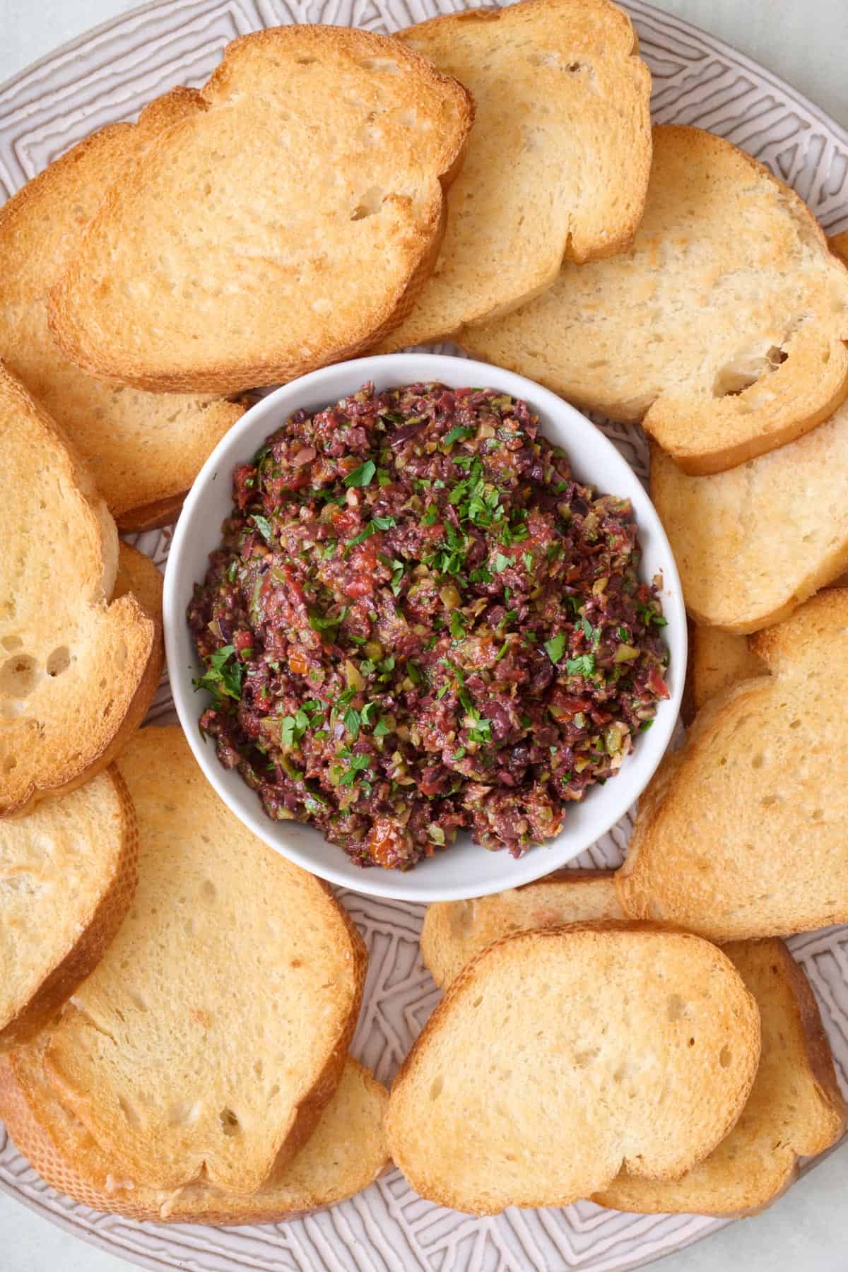 Olive tapenade in a serving bowl on a platter with small toasts.