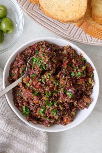 Olive tapenade in a bowl with small toasts nearby.