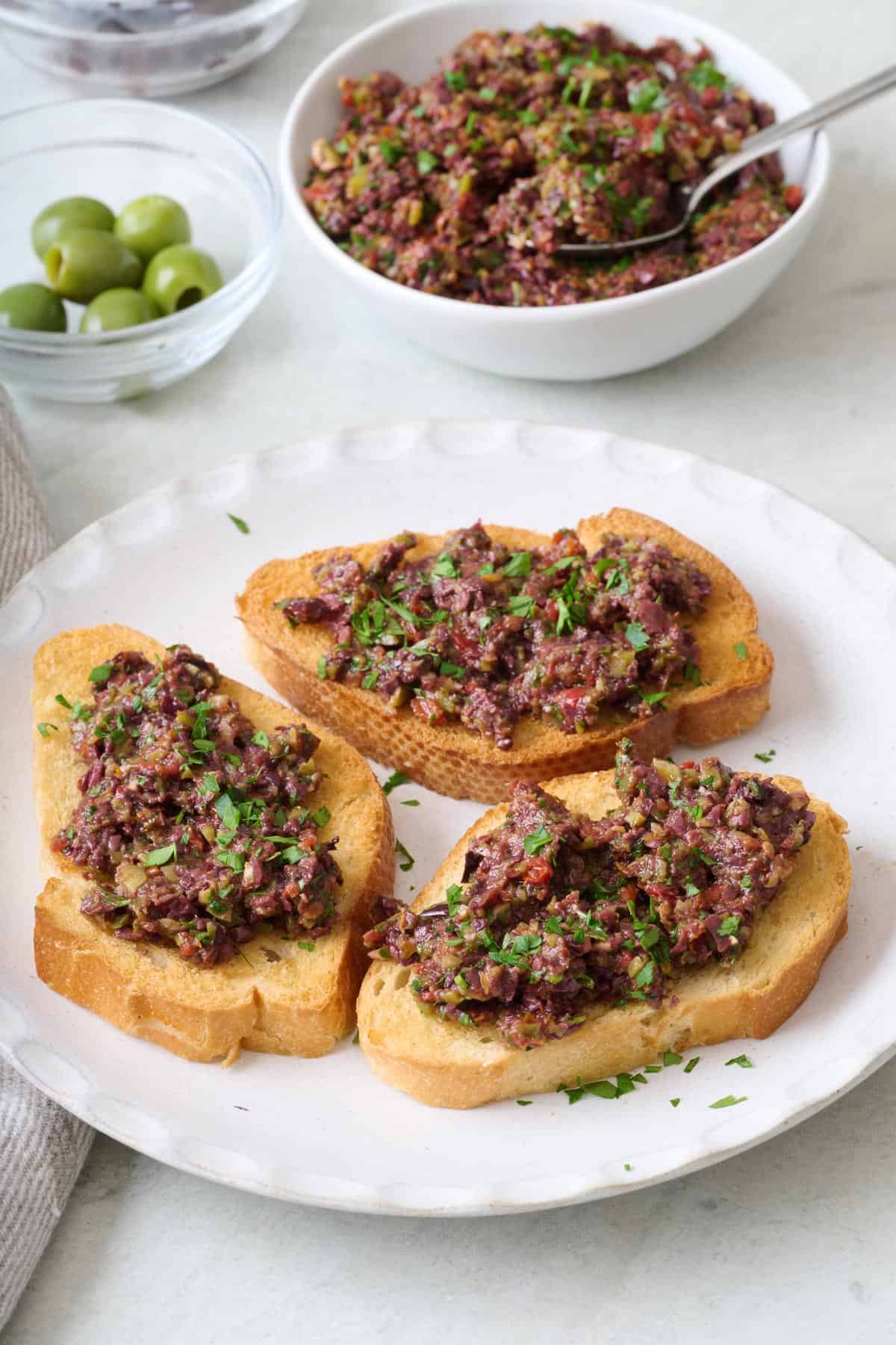 Olive tapenade on a few pieces of toasts with a bowl of more nearby.