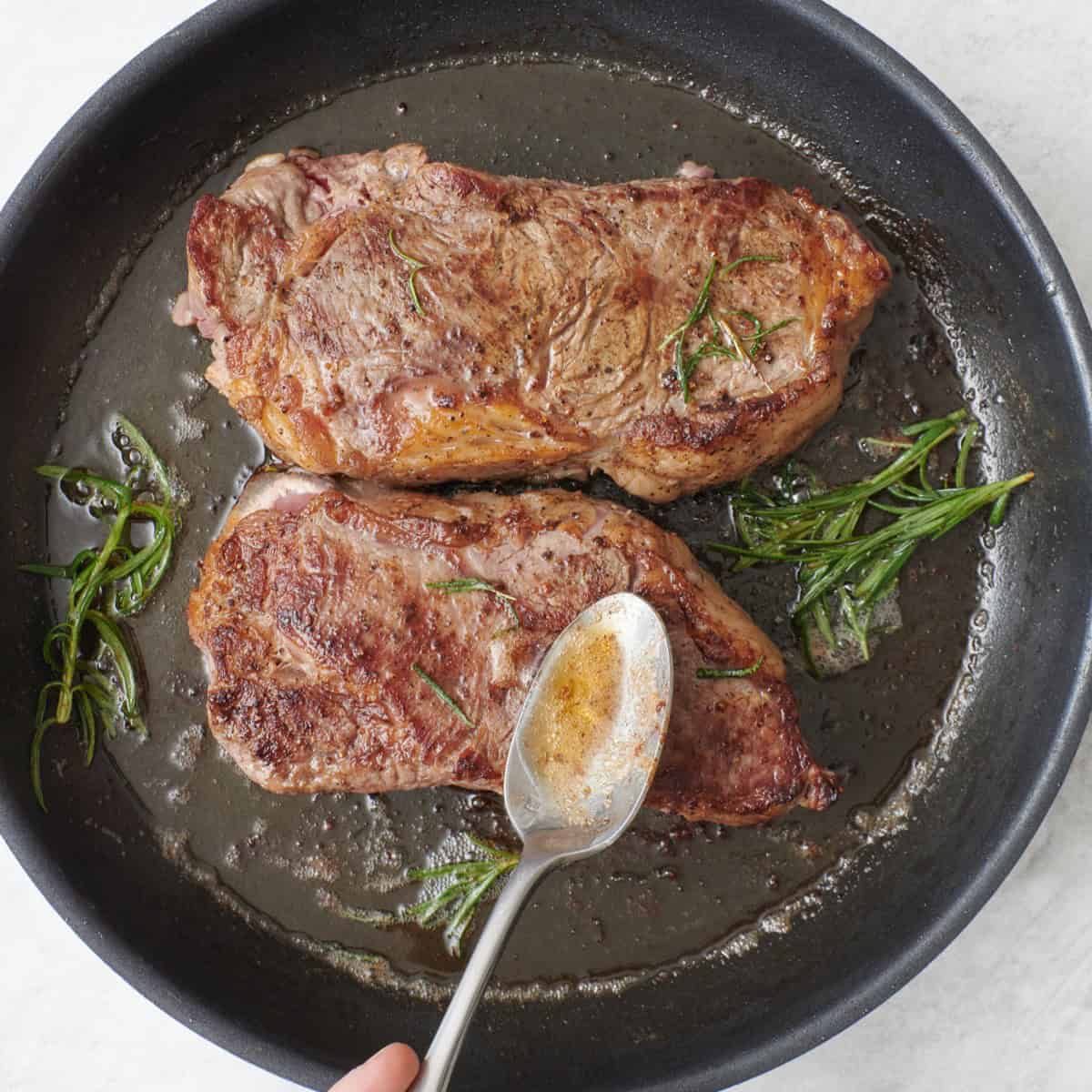 Spooning butter over the pan seared steaks.