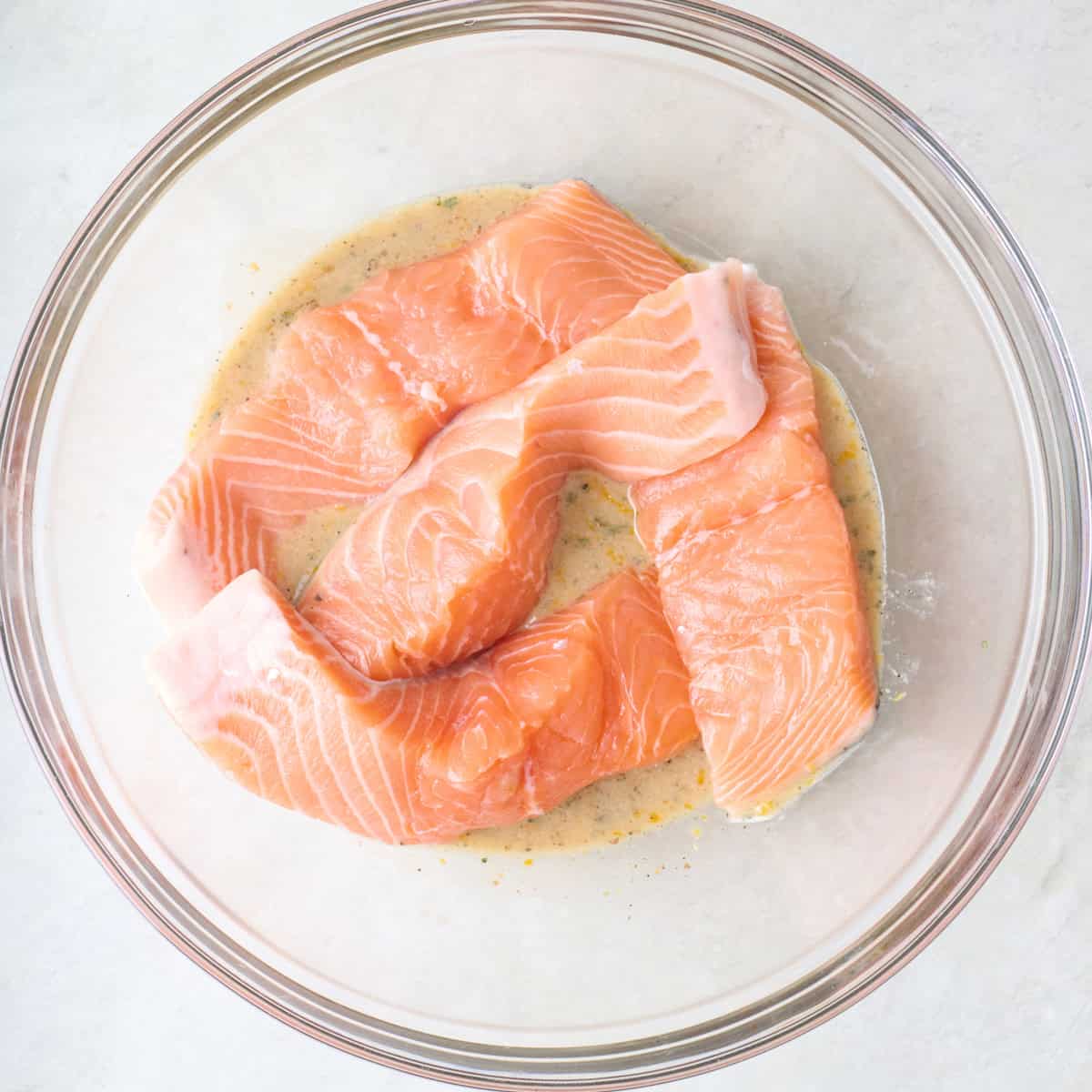 Salmon fillets on top of marinade in a bowl.