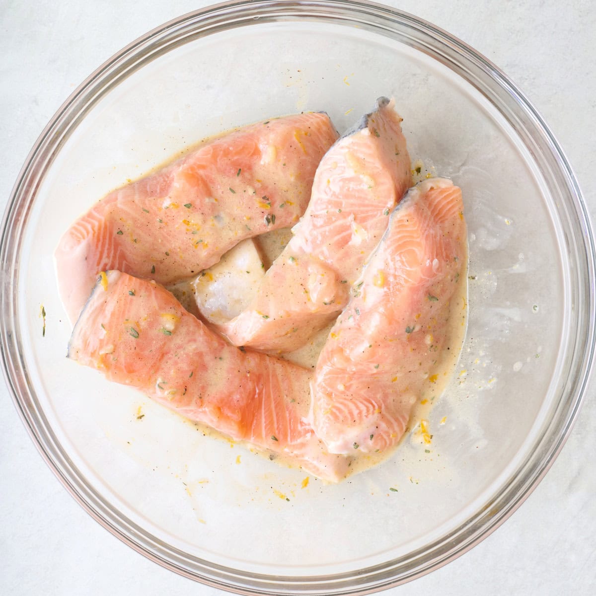 Salmon fillets tossed in a mustard marinade in a bowl.