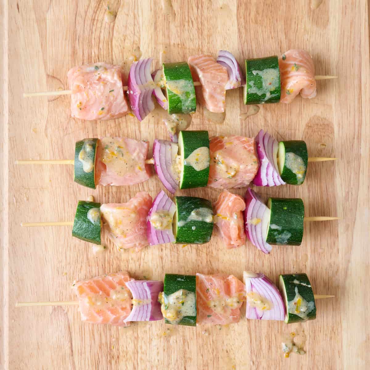 Marinated salmon bites threaded on a skewer with sliced zucchini and red onion chunks.