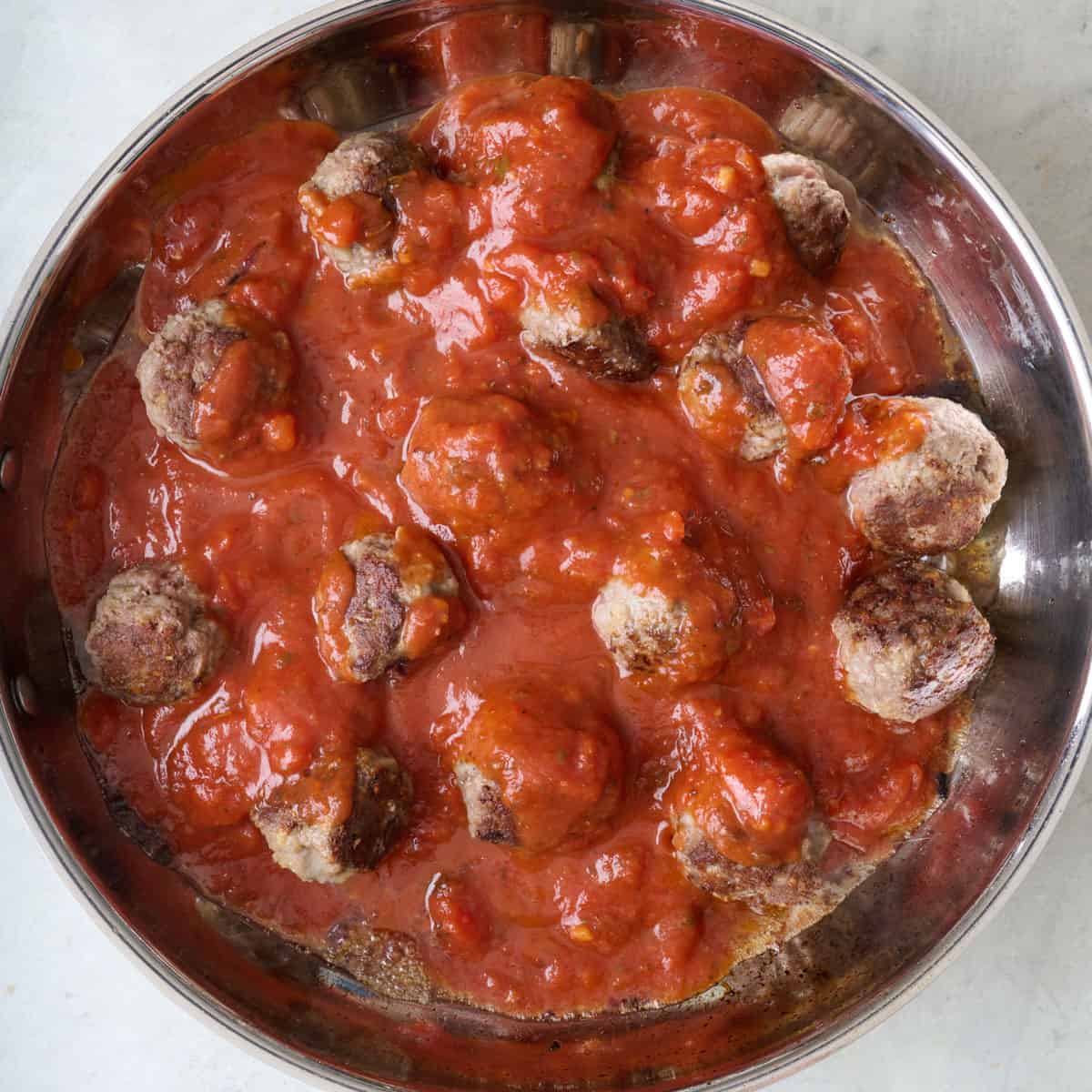 Tomato sauce added to skillet with cooked meatballs.