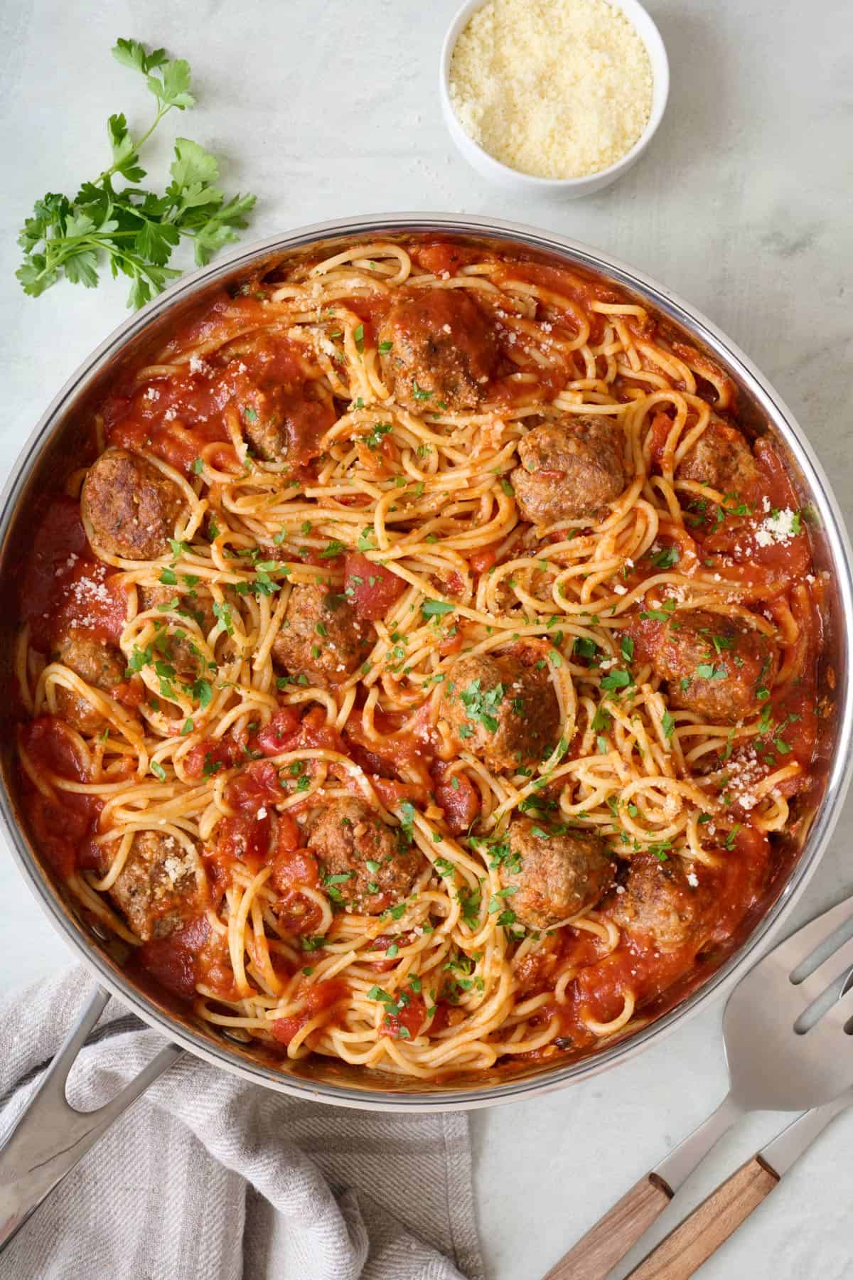 Spaghetti and meatballs in a skillet, garnished with fresh herbs and parmesan.