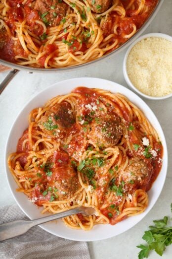 A serving of meatballs and spaghetti in a bowl with skillet of more nearby.