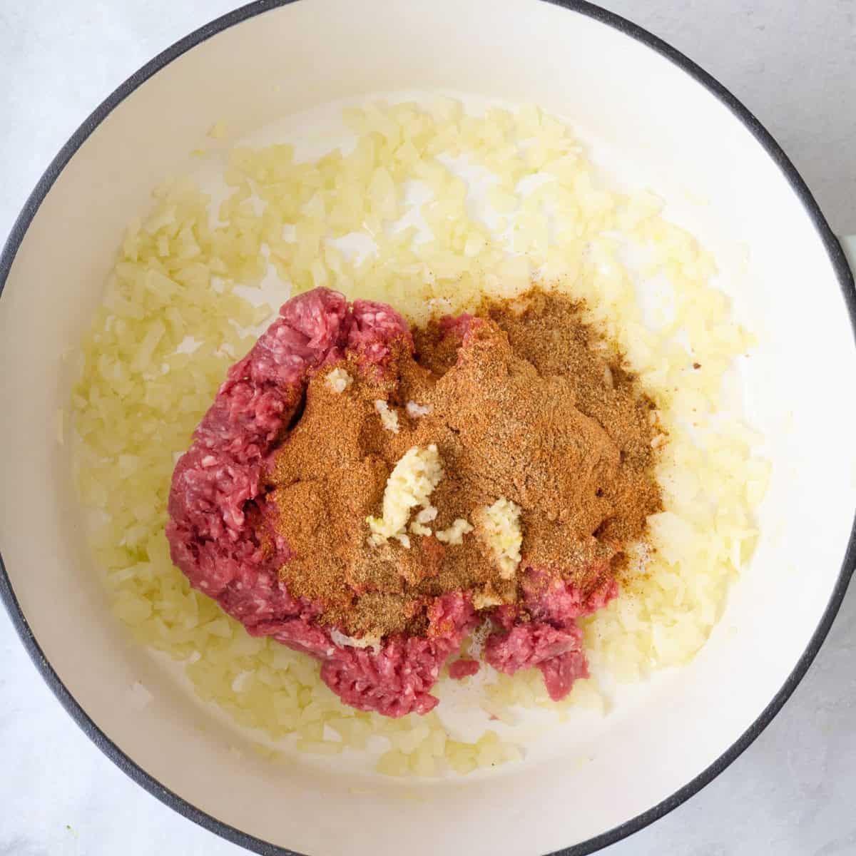 Seasoning, garlic, and beef added to the pan.