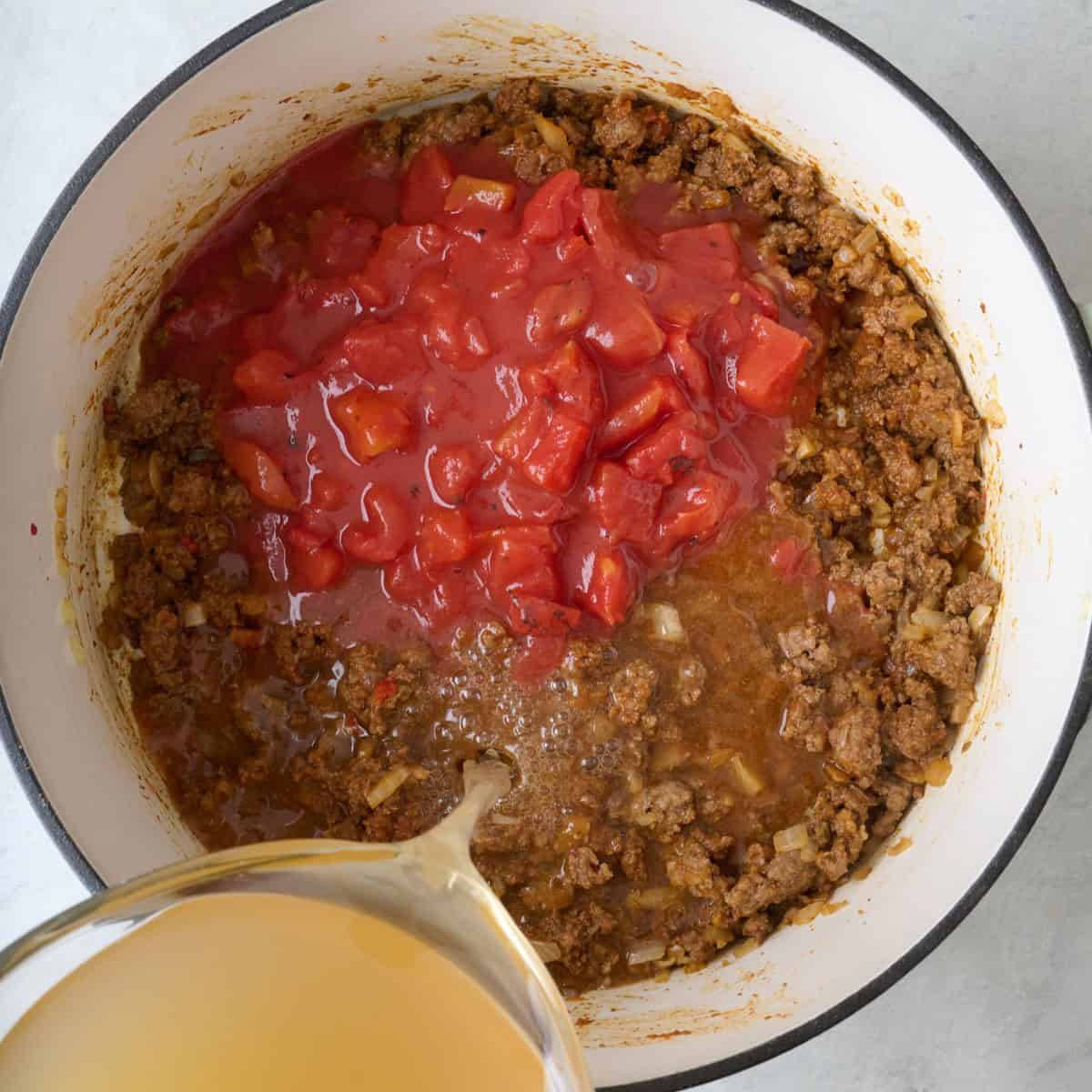 Diced tomatoes added to the beef mixture and stock being poured on top.