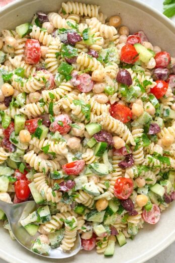 Tahini pasta salad in a large bowl with dressing and ingredients nearby.