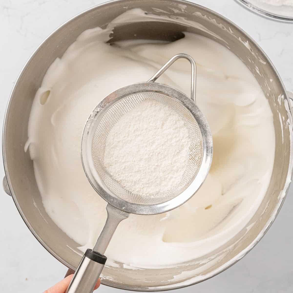 Flour, salt, and sugar being sifted into a bowl.