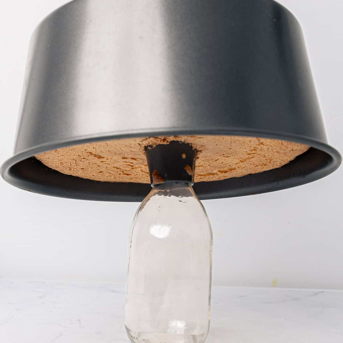 The cake pan rested on top of a bottle to cool.