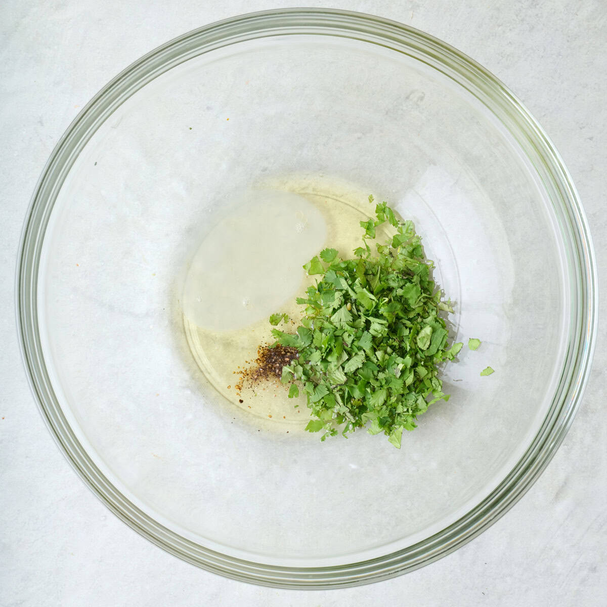 Chopped cilantro, olive oil, lime juice, salt, and pepper in a mixing bowl.