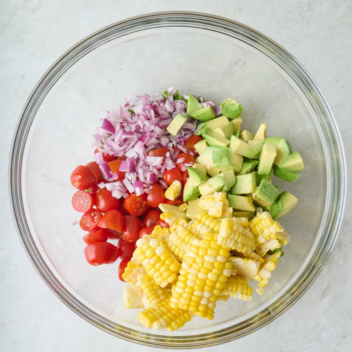 Diced red onion, cubed avocado, halved cherry tomatoes, and corn kernels in a larg emixing bowl.