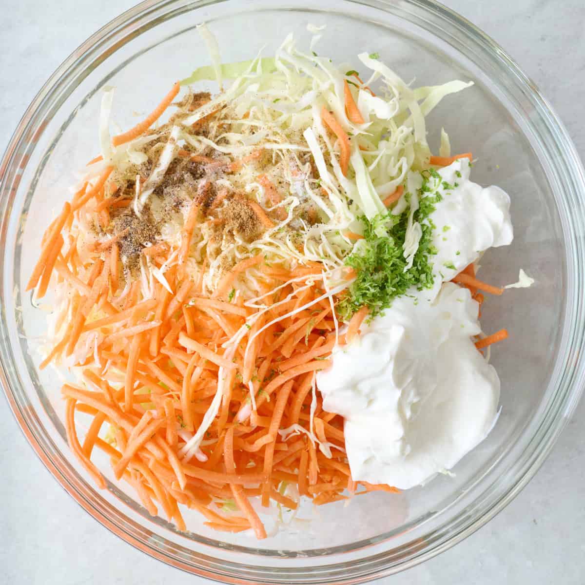 Shredded cabbage, carrots, and a Greek yogurt dressing in a large glass bowl.