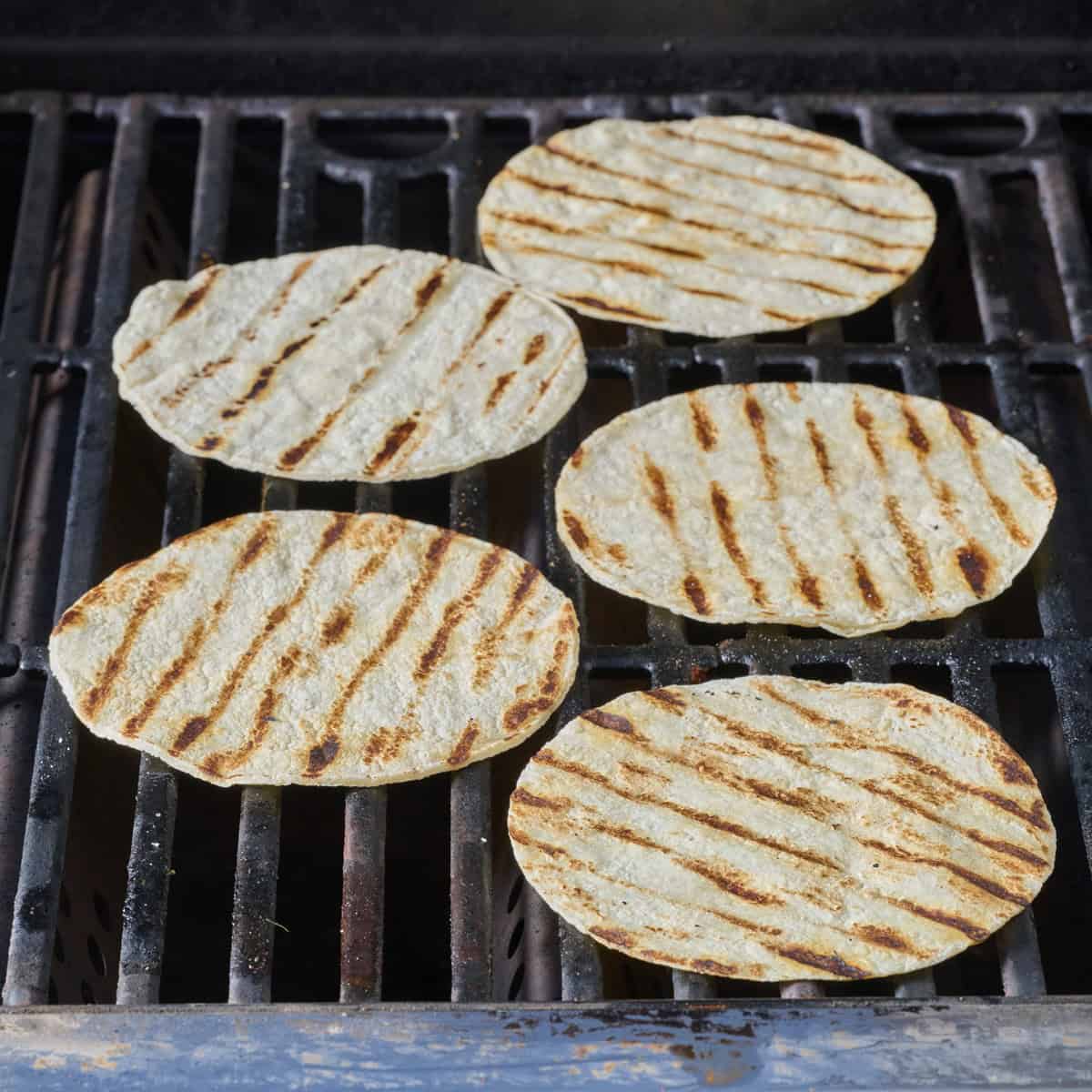 Five browned tortillas on a gas grill.