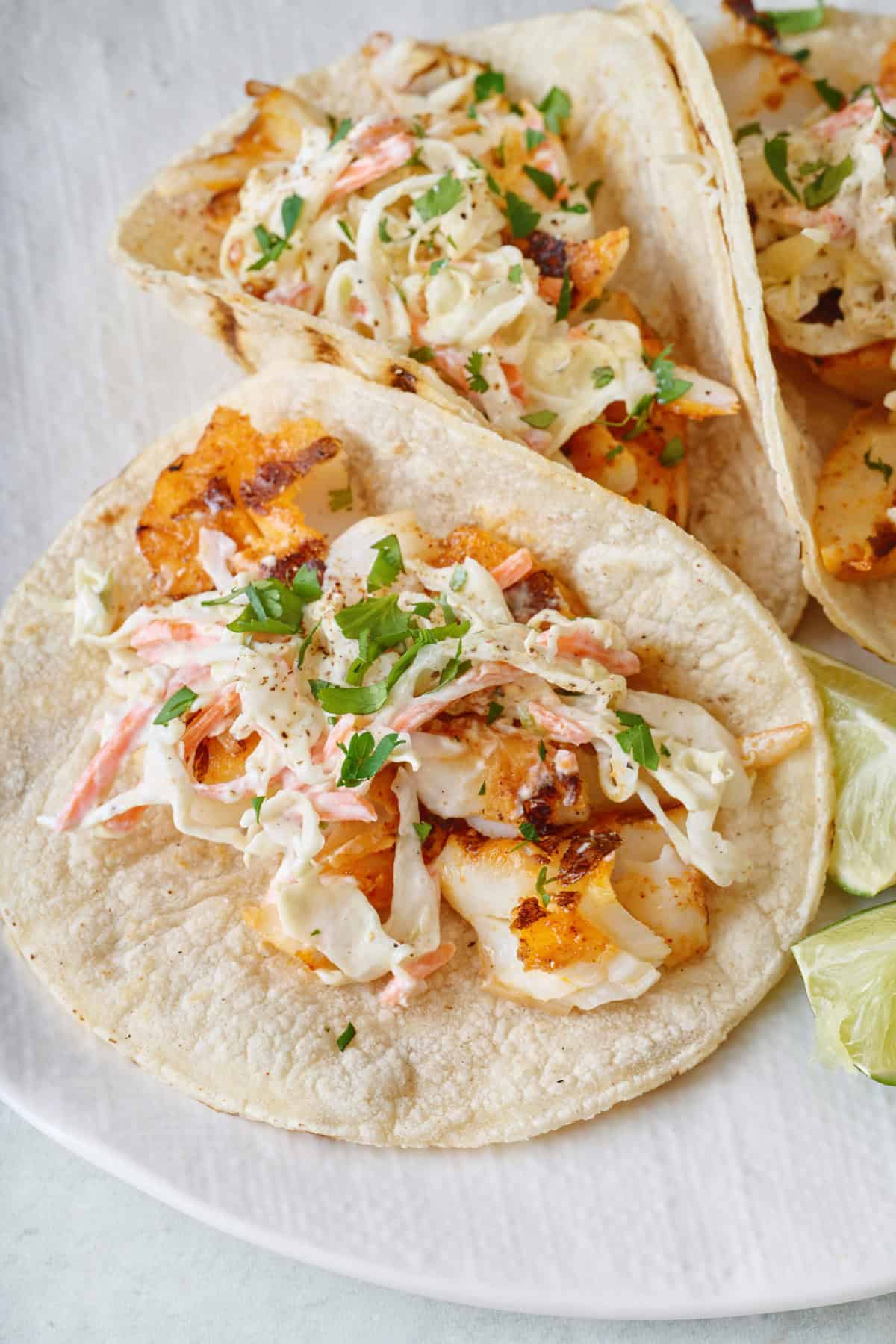 Grilled fish tacos topped with coleslaw and chopped cilantro on a plate.