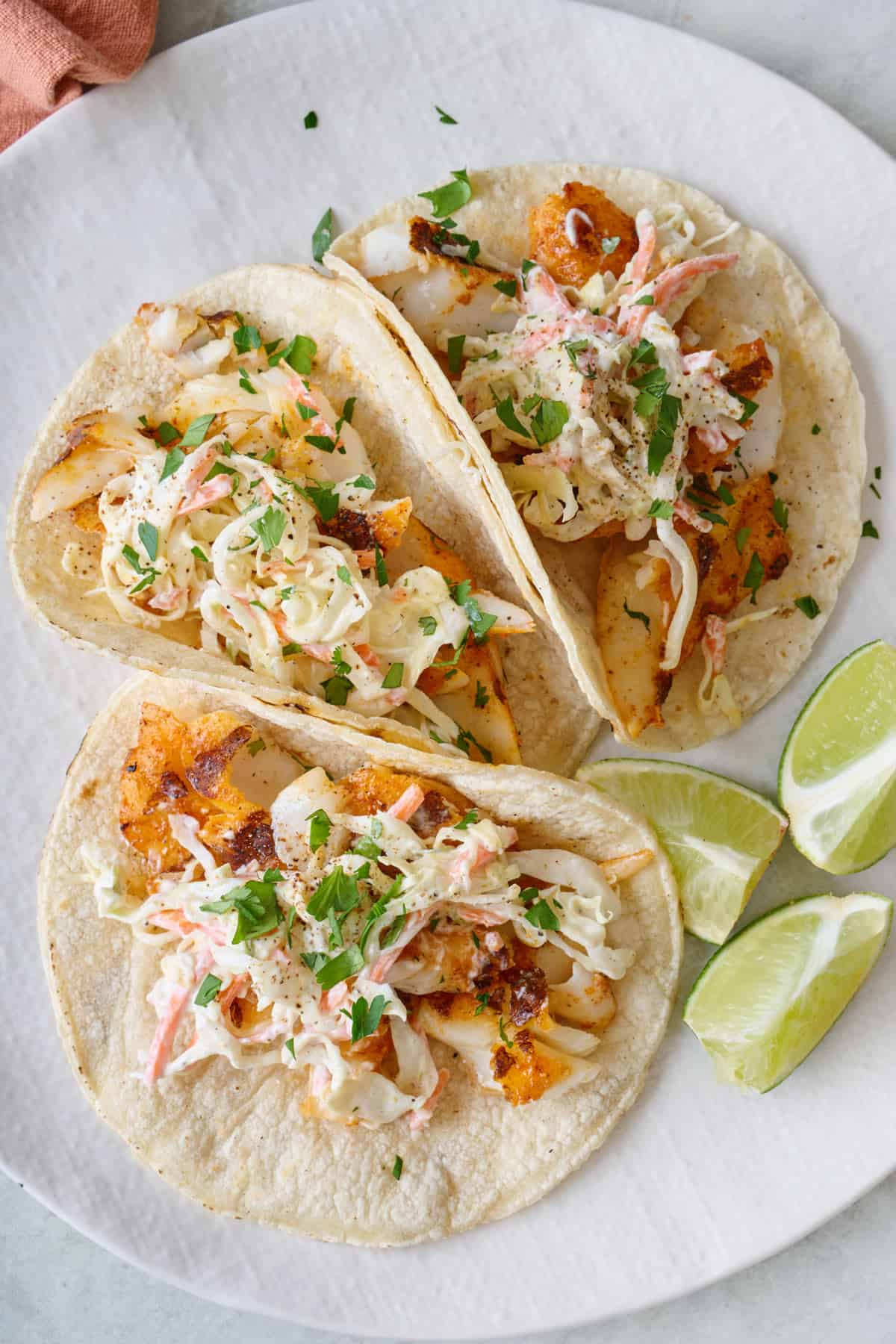 Three grilled fish tacos topped with coleslaw and topped cilantro on a plate.