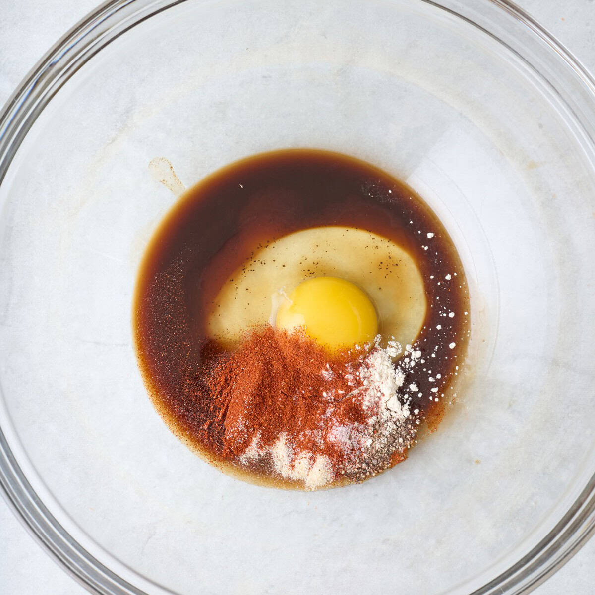 Worcestershire sauce, spices, and an egg in a mixing bowl.