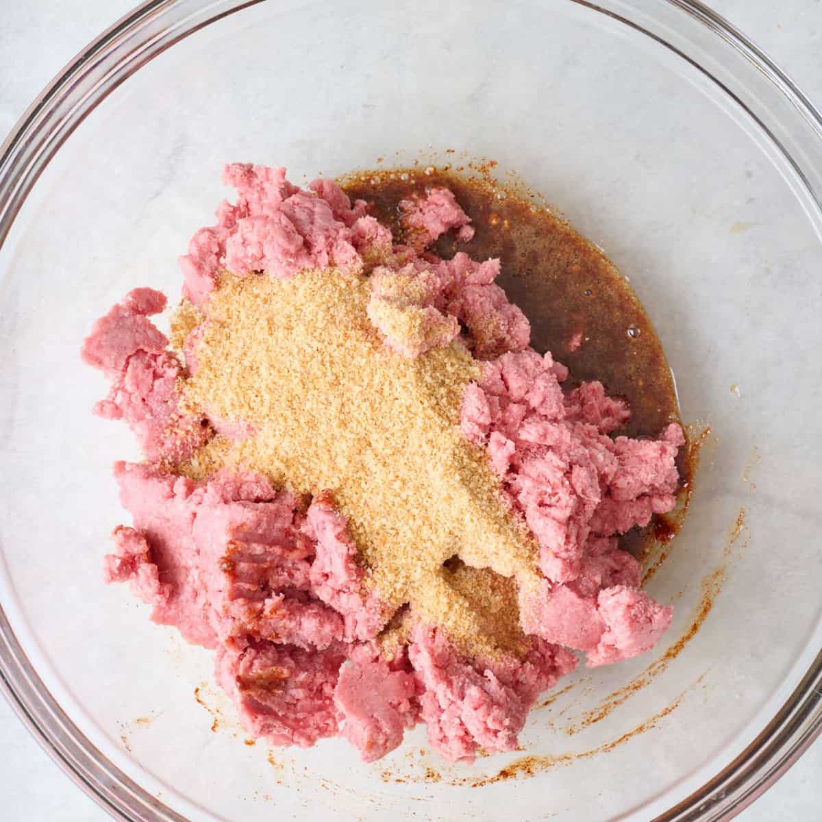 Ground beef, breadcrumbs, and seasonings in a mixing bowl.