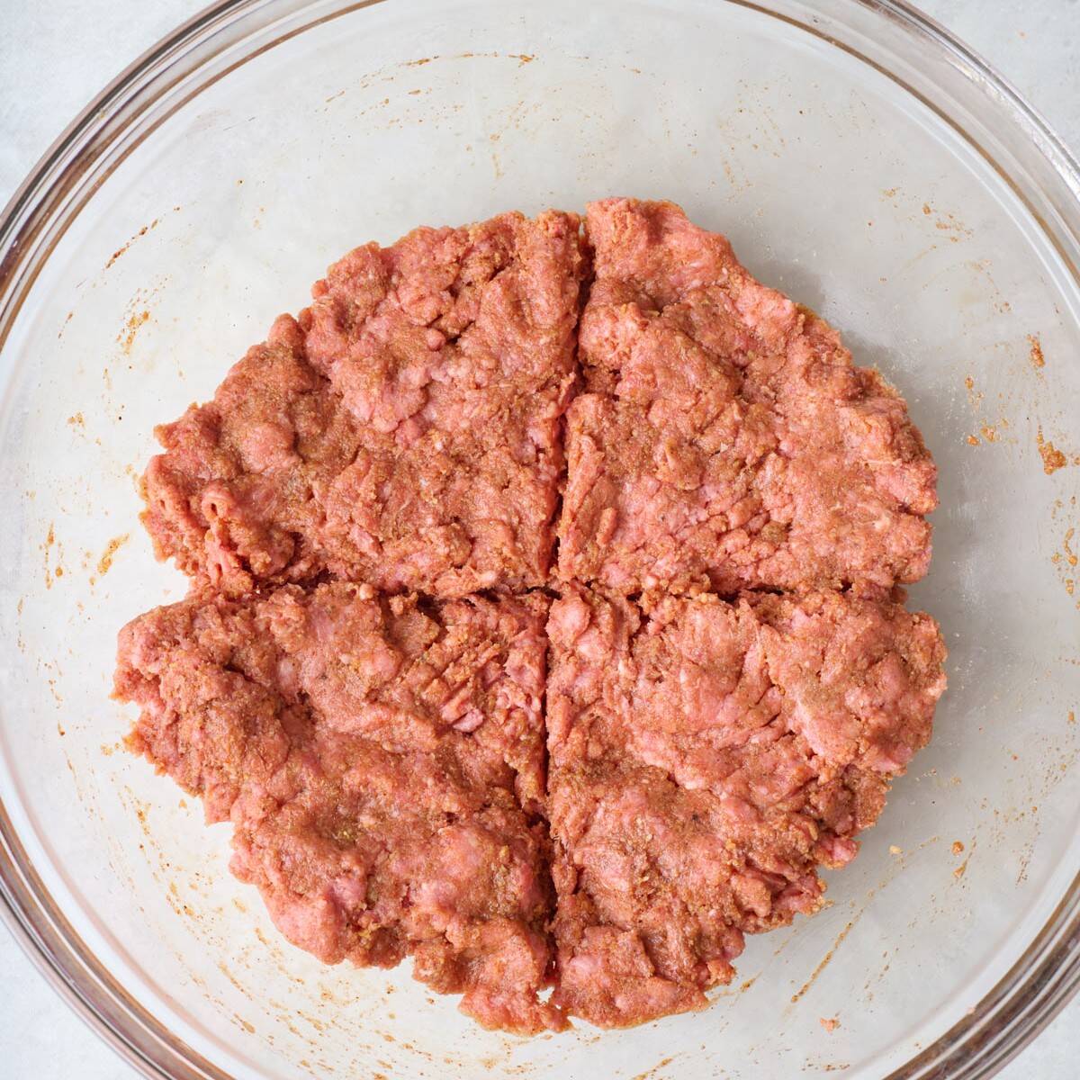 Hamburger patty mixture divided into four sections in a mixing bowl.