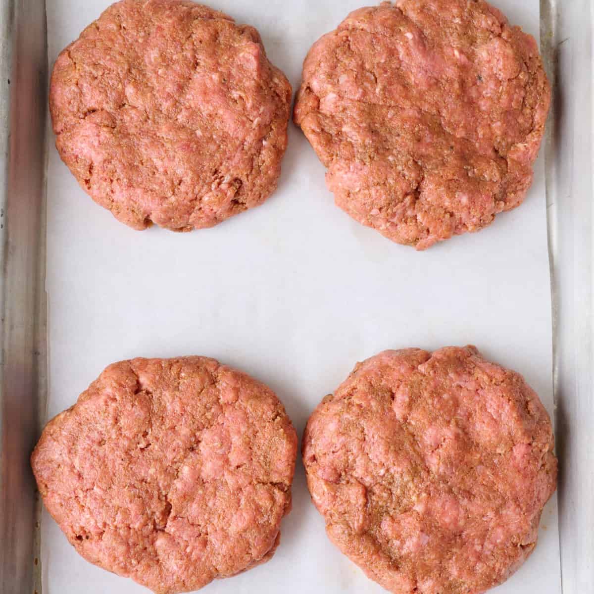 Four hamburger patties on a parchment-lined baking sheet.