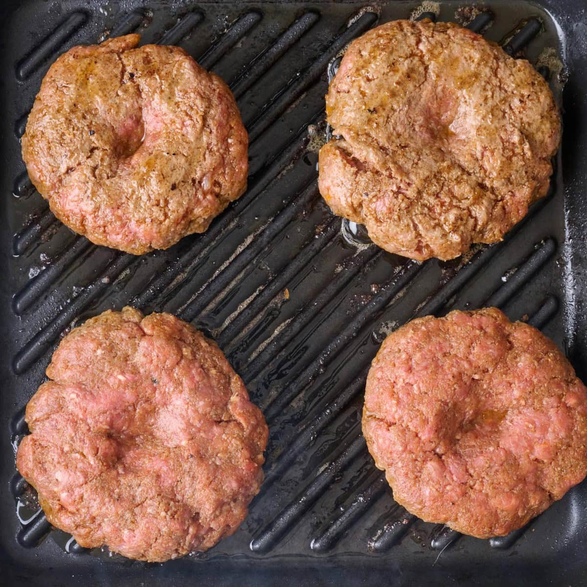 Four hamburger patties cookies on a grill pan.