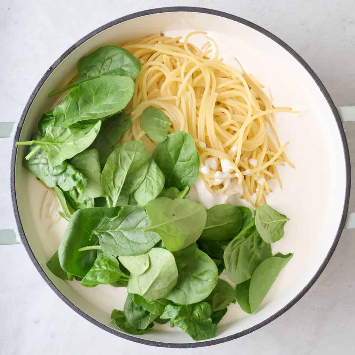Cooked spaghetti, lemon ricotta pasta sauce, and baby spinach in a pot.