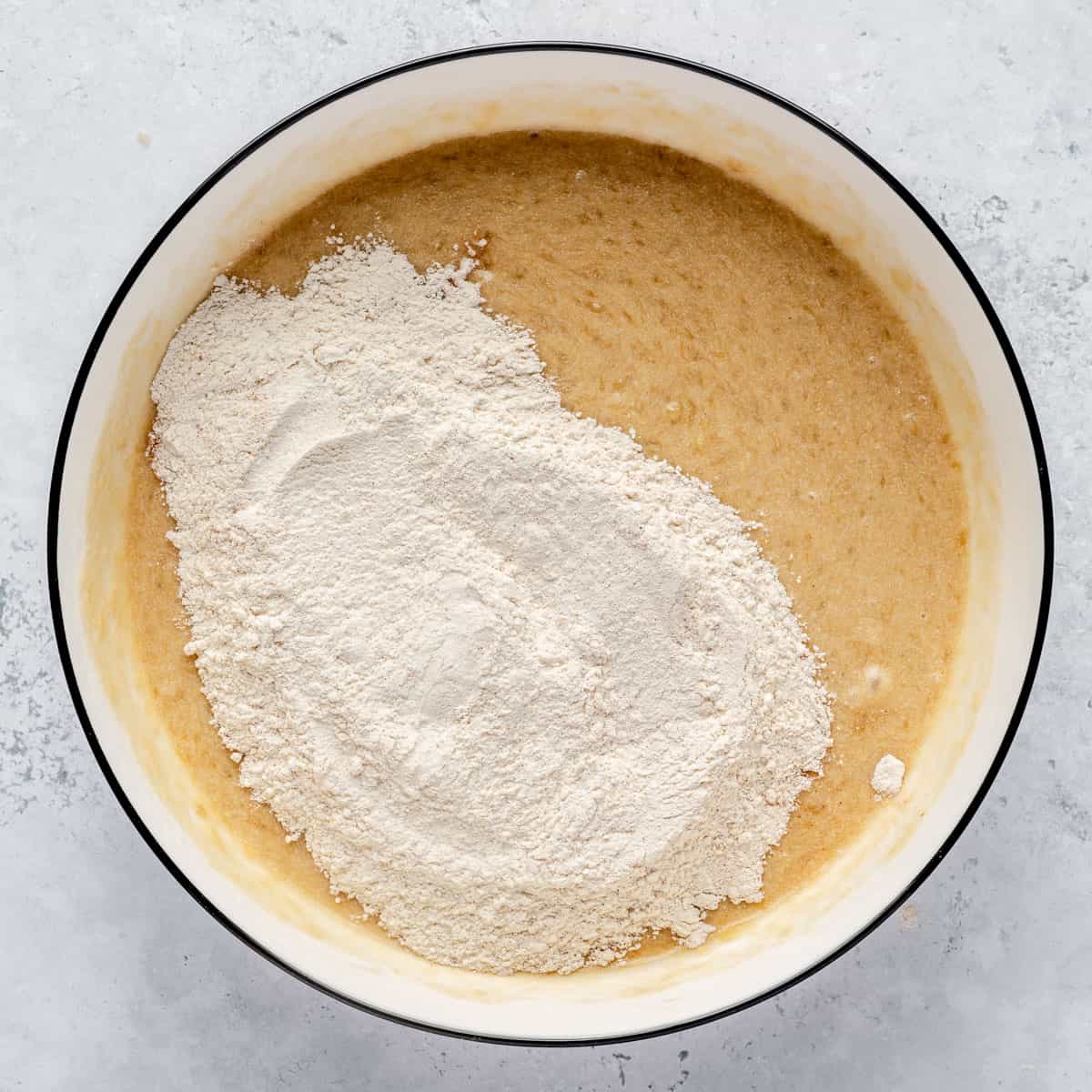 Wet ingredients and dry ingredients for mini banana muffins in a mixing bowl.