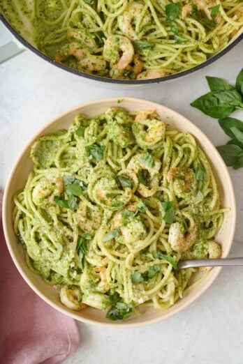 A bowl of shrimp pesto pasta with a fork dipped inside and the pot of more nearby.