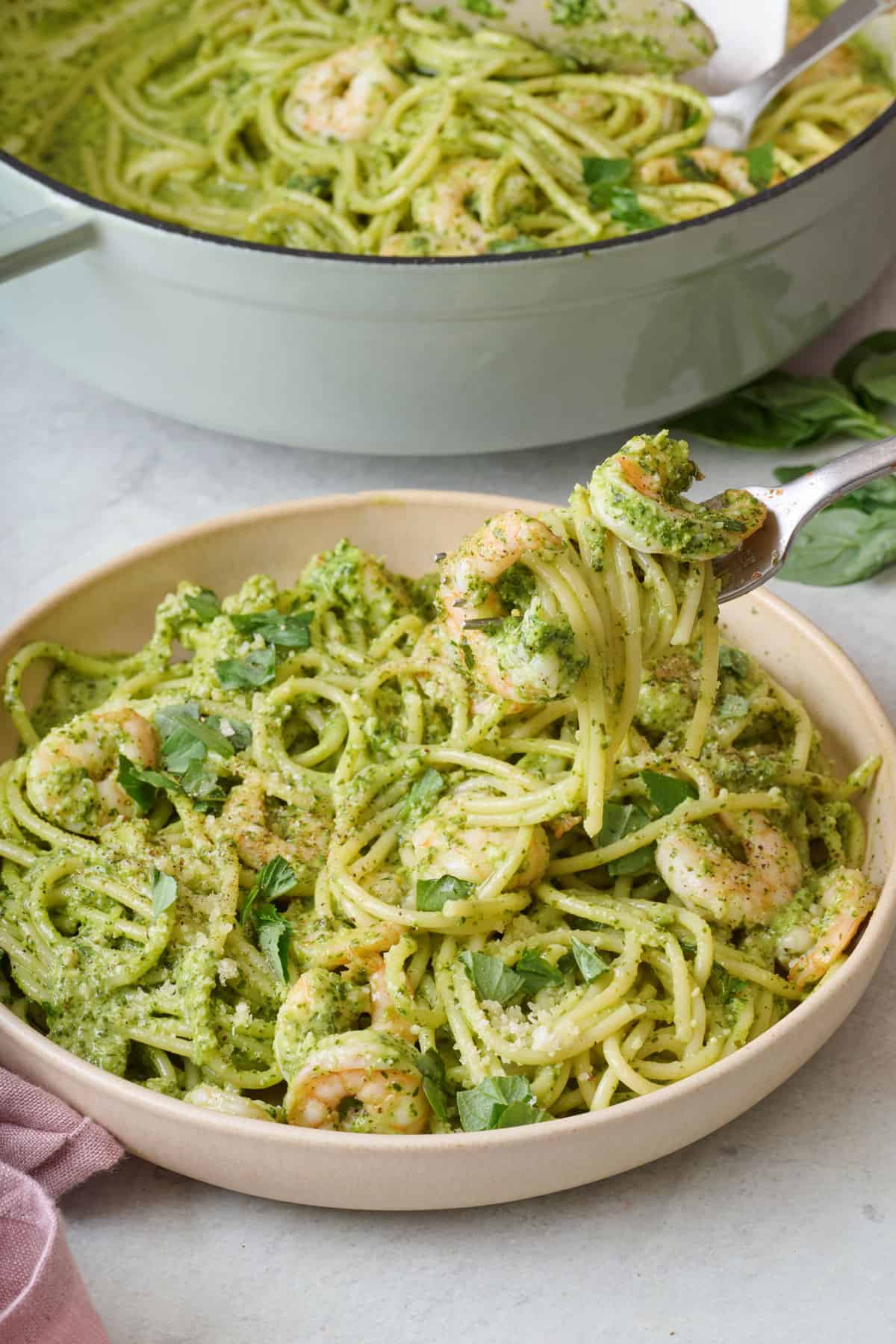 A bowl of shrimp pesto pasta with a fork lifting up a bite and the pot of more nearby.