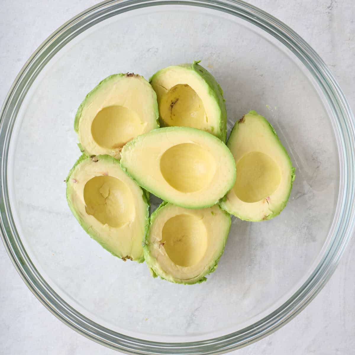 Avocado halves in a large glass mixing bowl.